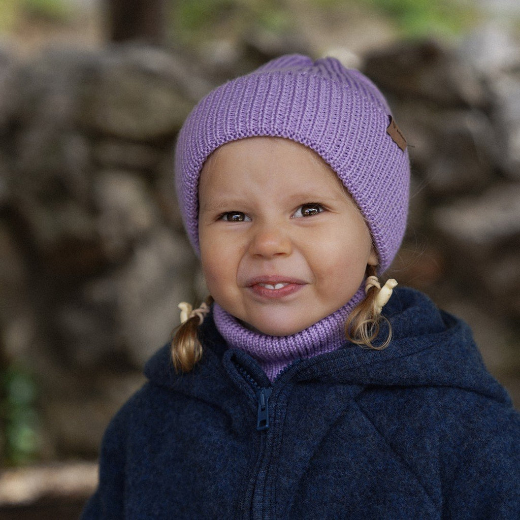 3. Smiling child in lavender merino wool hat and neck warmer, wearing blue jacket, outdoors