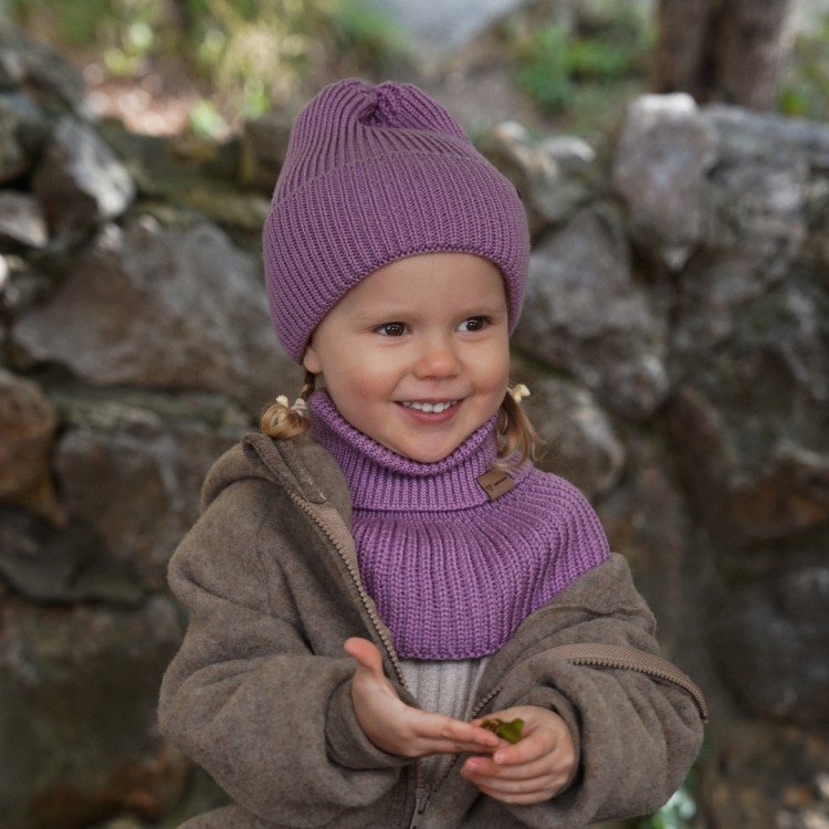 7. Child in lilac merino wool hat and scarf wearing brown coat outdoors with stone background