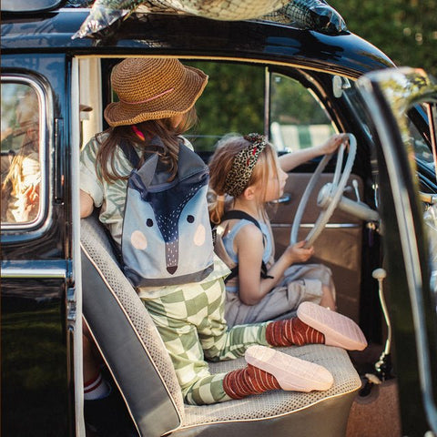 3. Two children with Muni wolf backpacks in a car, emphasizing fun and exploration