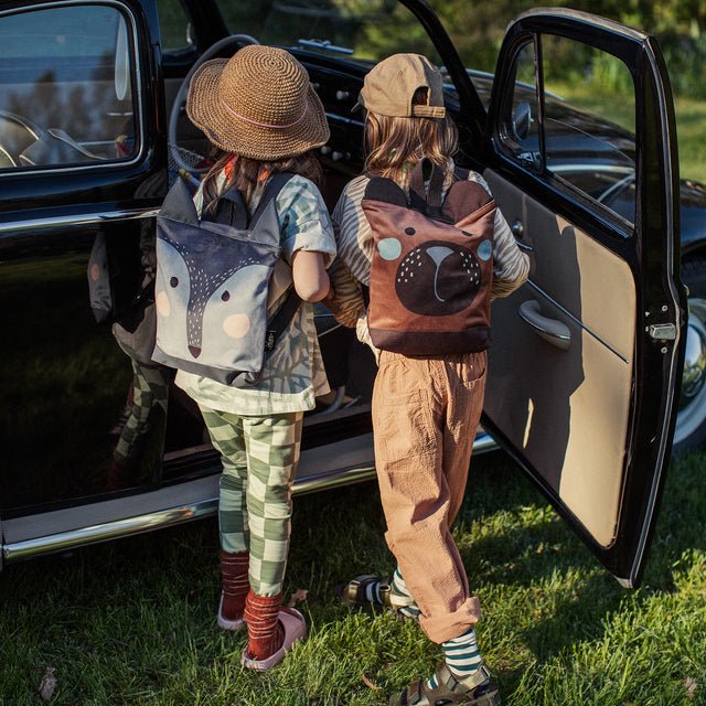 6. Two children with Muni wolf backpacks standing by a car, ready for adventure