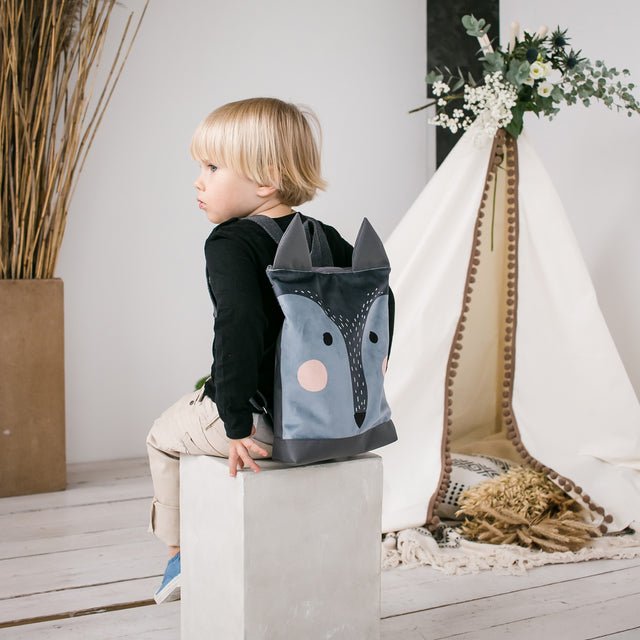 7. Child sitting with Muni wolf backpack in a studio setting, showcasing design