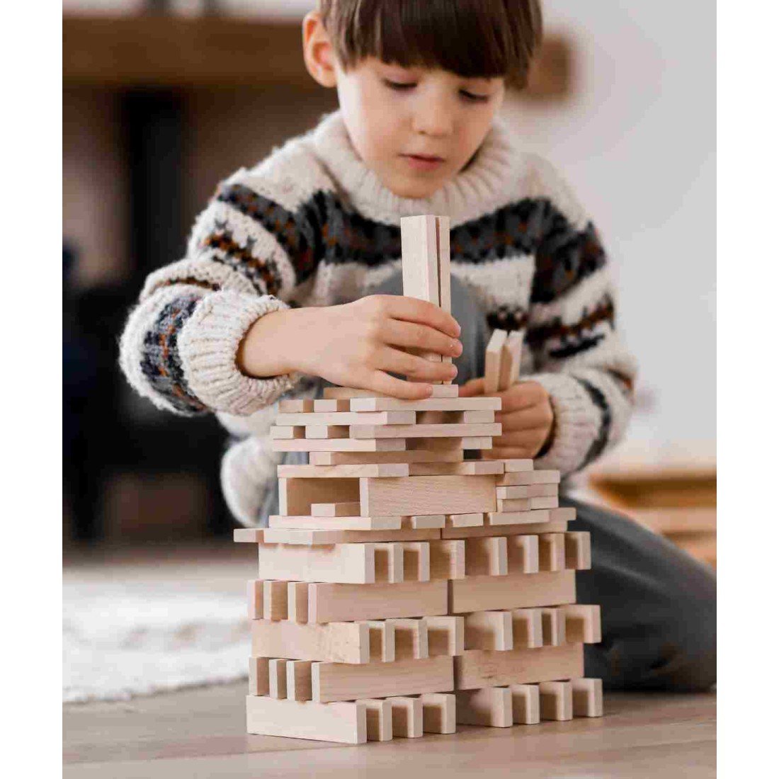 1. Boy constructing with Wooden Story blocks, focusing on tower structure, wearing a sweater indoors