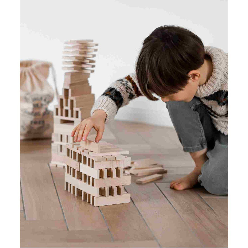 1. Young boy playing with Wooden Story architectural blocks on wooden floor, building a structure with natural wood pieces