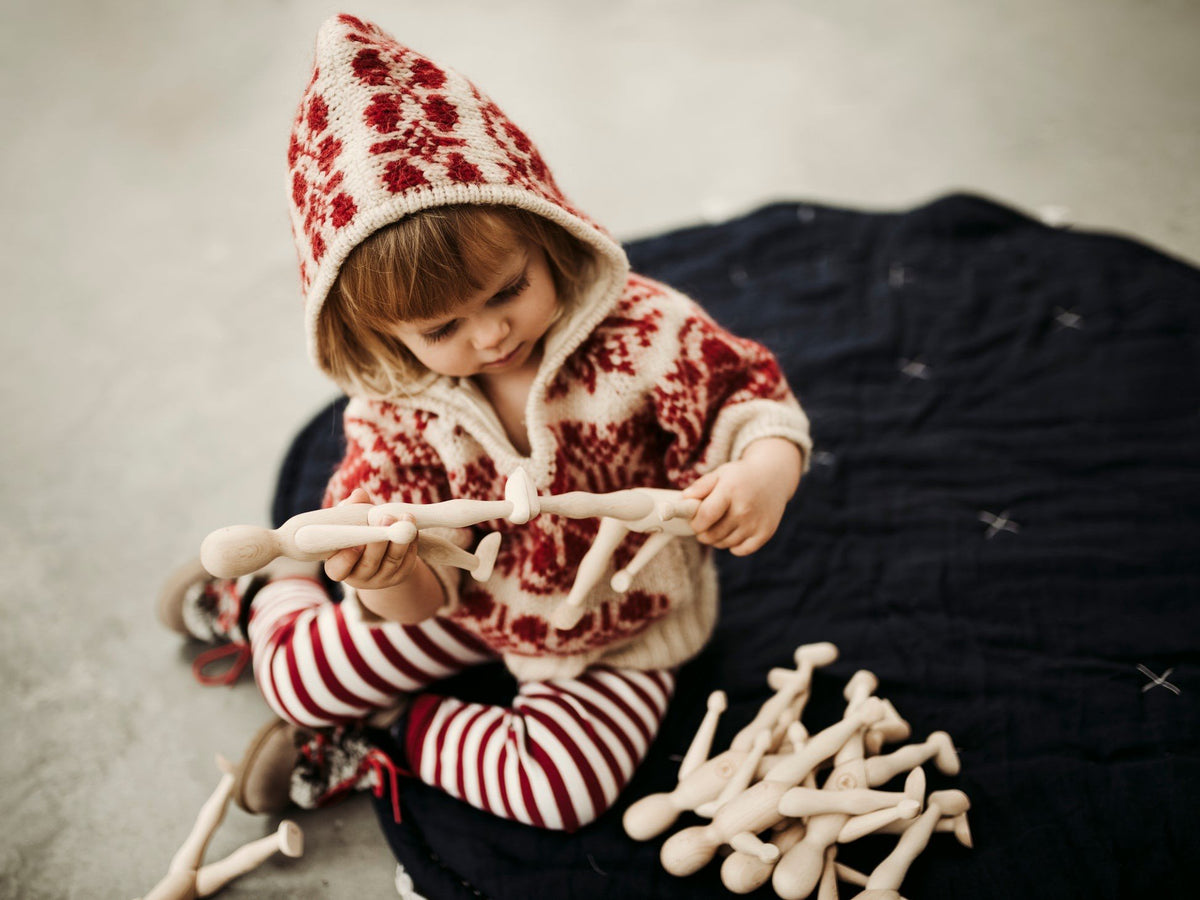 1. Child in a red patterned hoodie playing with multiple wooden beech dolls