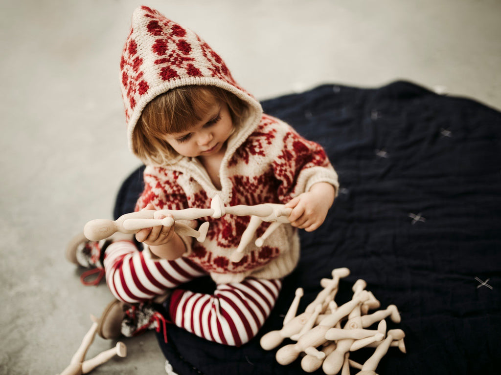 8. Child in red patterned sweater playing with multiple Wooden Story beech dolls on blanket