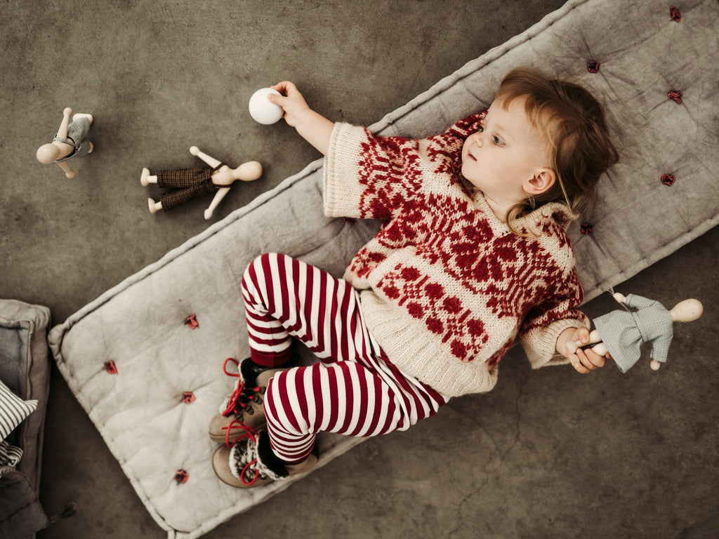 10. Child in red patterned sweater lying on cushion holding Wooden Story beech dolls