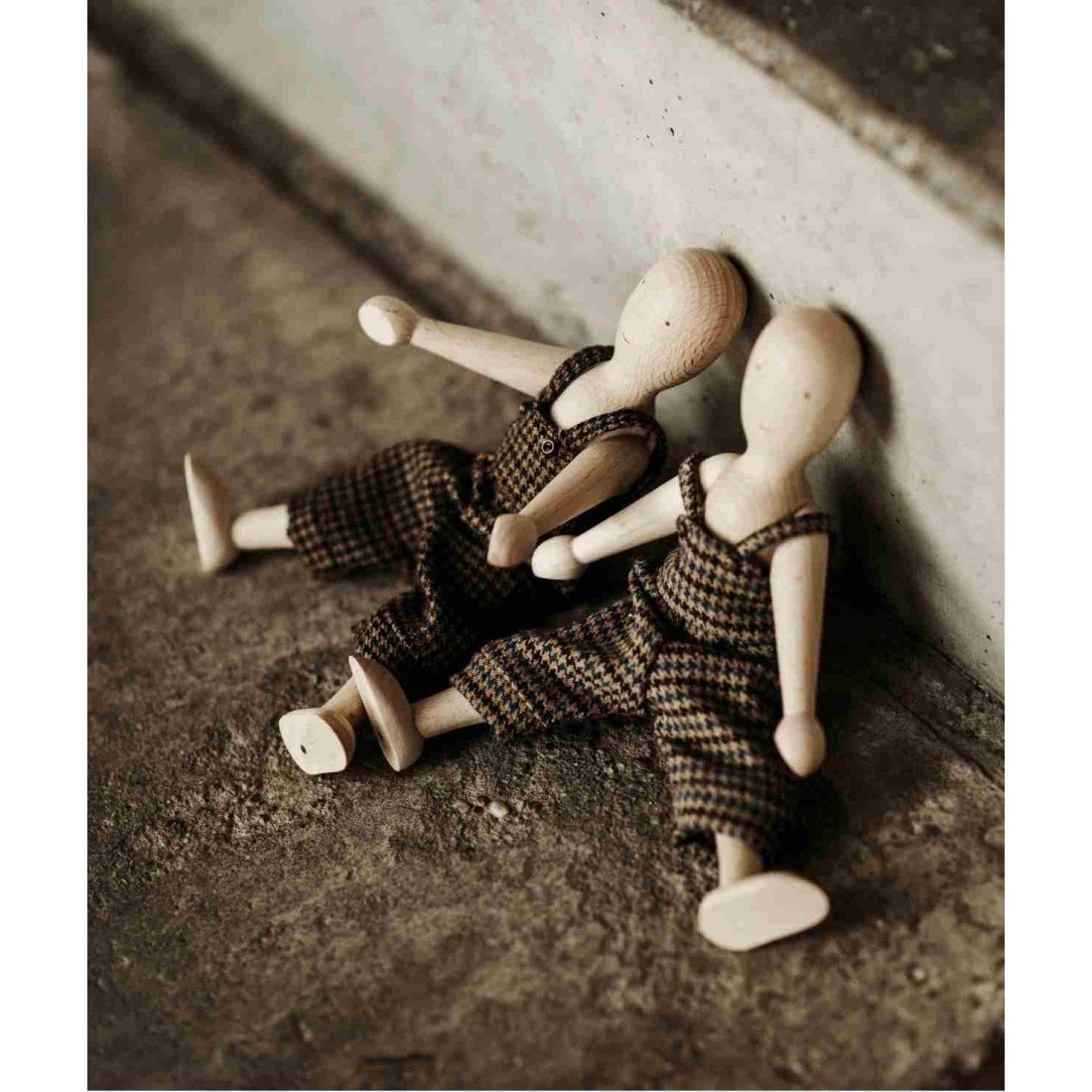 1. Two wooden beech dolls with pants sitting against a wall on a textured surface