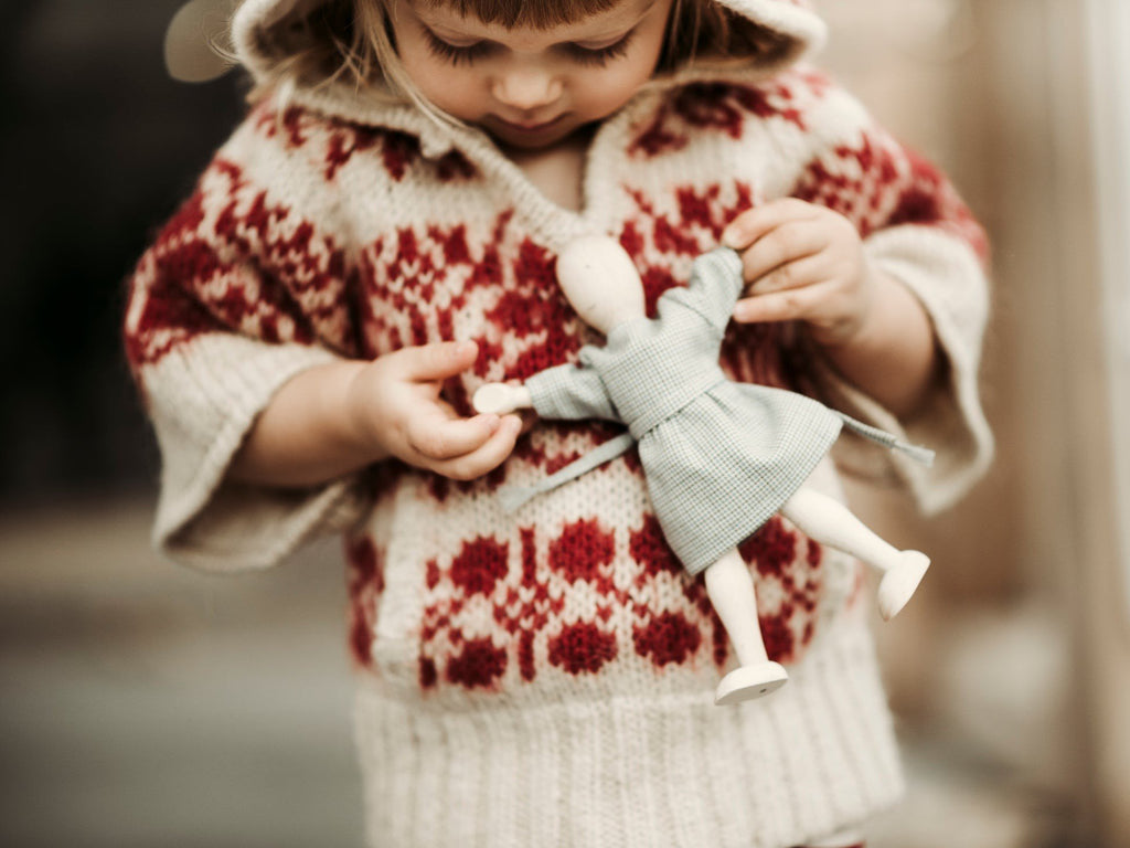 1. Child in a red patterned sweater holding a wooden beech doll