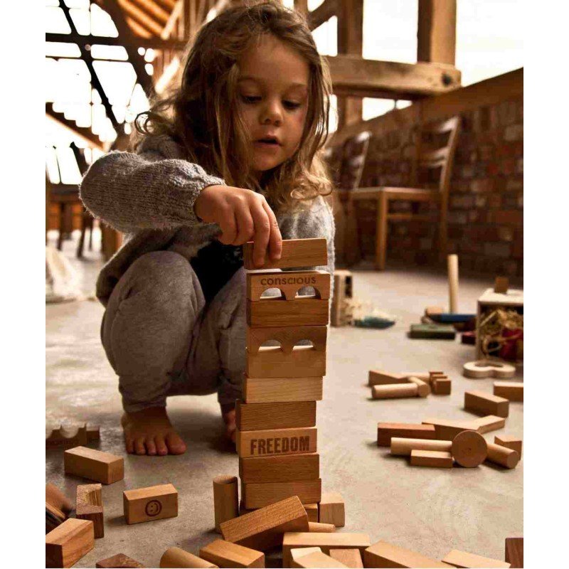 1. Young girl building a tower with Wooden Story natural wooden blocks in a rustic setting, promoting creativity and motor development