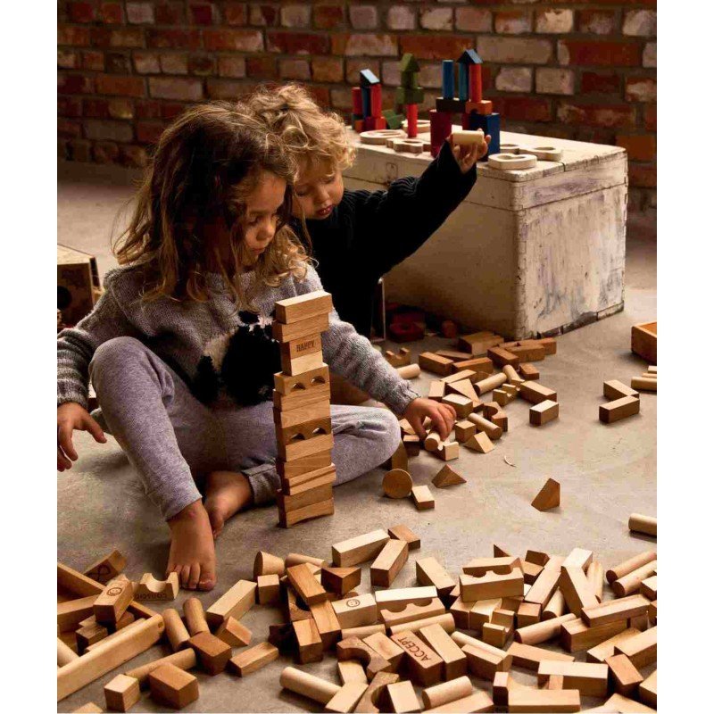 1. Two children playing with Wooden Story natural wooden blocks in a cozy room with brick walls, engaging in creative play and building structures