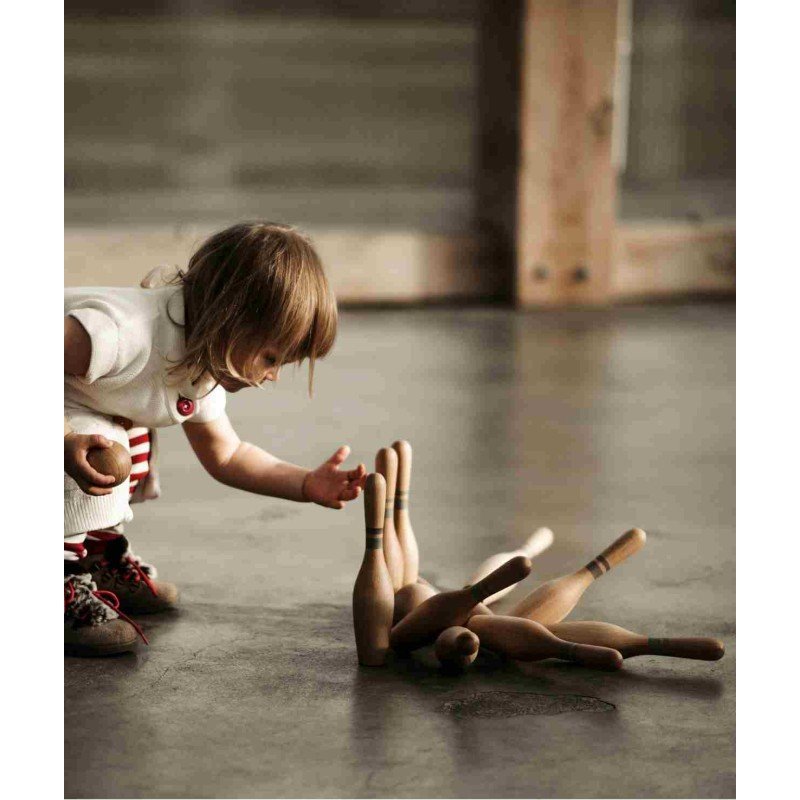 1. Child in white dress picking up fallen wooden bowling pins on a wooden floor