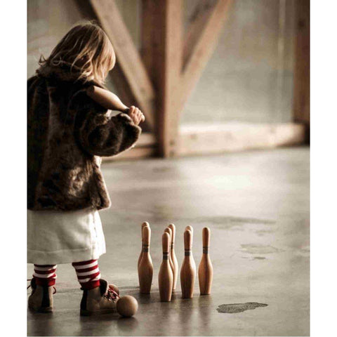 1. Child in striped leggings setting up wooden bowling pins on a wooden floor