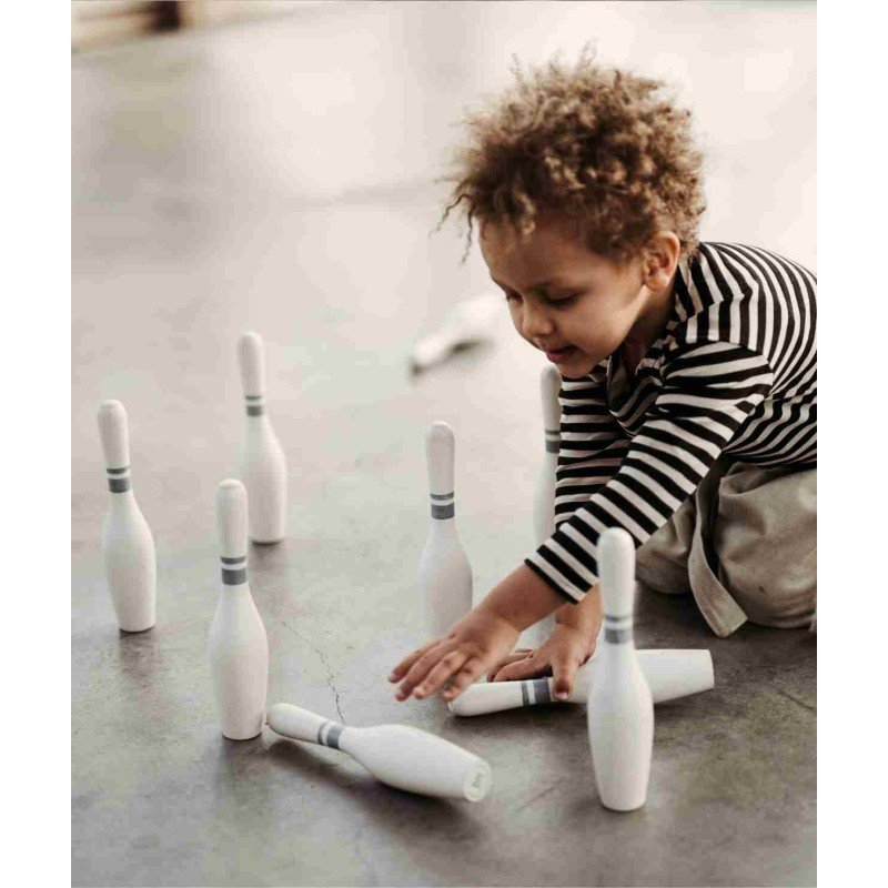 1. Child in striped shirt setting up wooden bowling pins on a concrete floor