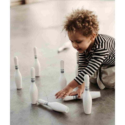1. Child in striped shirt setting up wooden bowling pins on a concrete floor