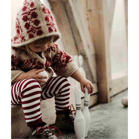 1. Child in red and white knitwear playing with wooden bowling pins indoors