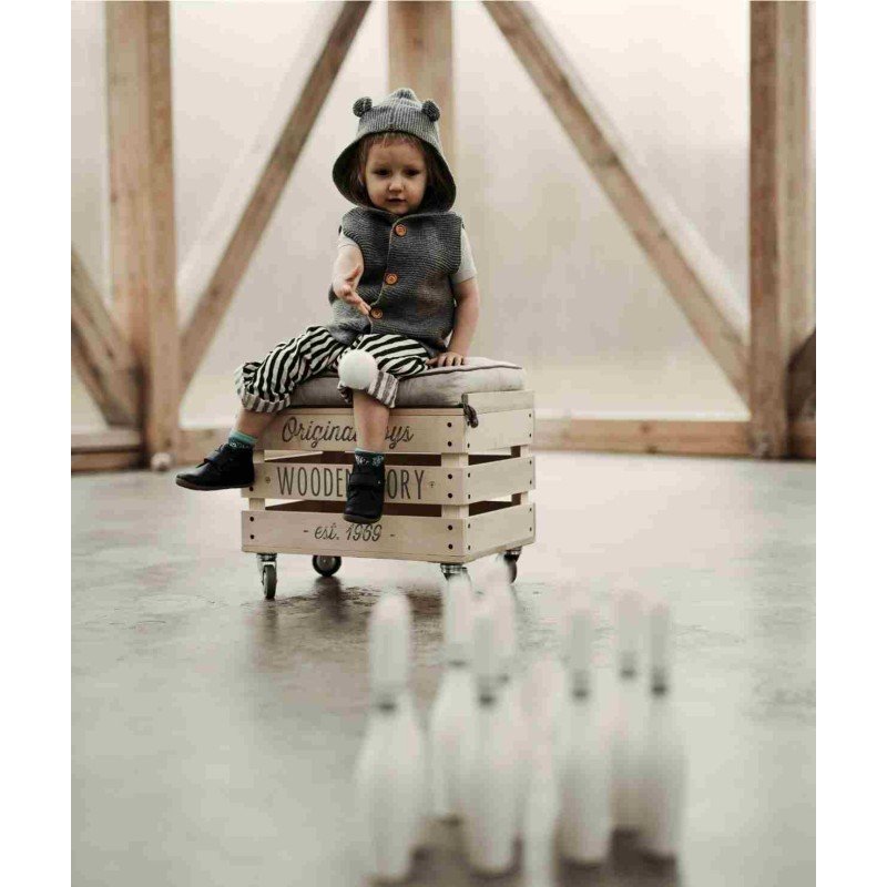 1. Child sitting on a wooden crate playing with wooden bowling pins indoors