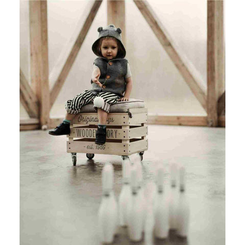1. Child sitting on a wooden crate playing with wooden bowling pins indoors