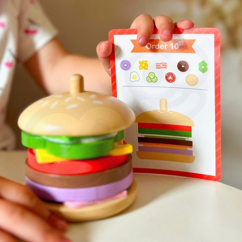 7. Child holding completed wooden burger puzzle with recipe card, highlighting colorful layers