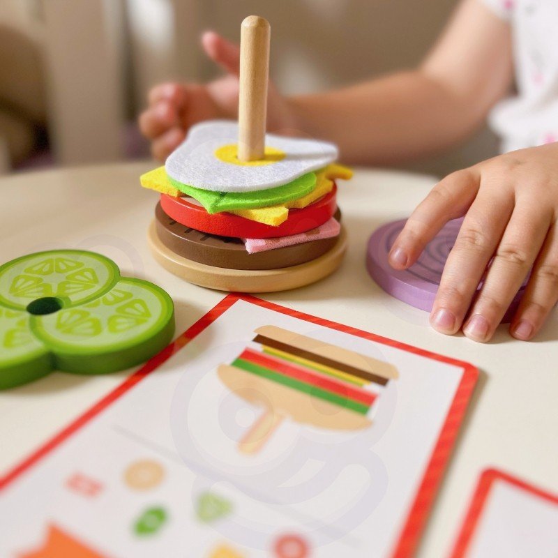 10. Child assembling wooden burger puzzle with colorful ingredients and recipe card on a table
