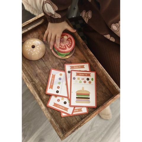 3. Close-up of child's hand assembling wooden burger puzzle with recipe cards on a wooden tray