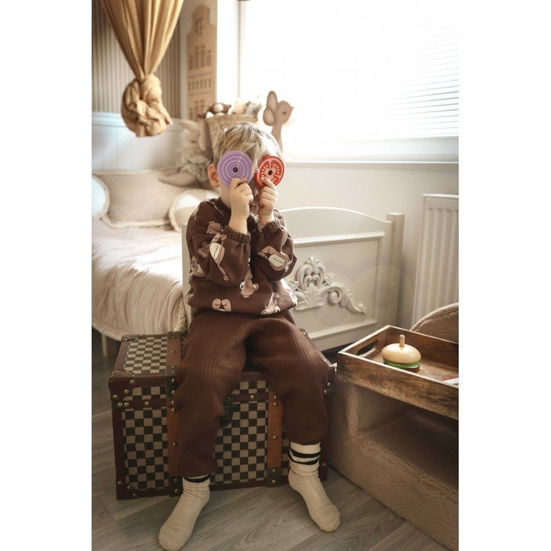 5. Child holding wooden burger puzzle pieces in front of face, sitting on a checkered trunk in a bedroom
