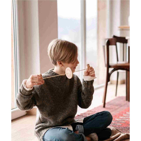1. Child in grey sweater playing with Wooden Buzz Spinner in a bright room
