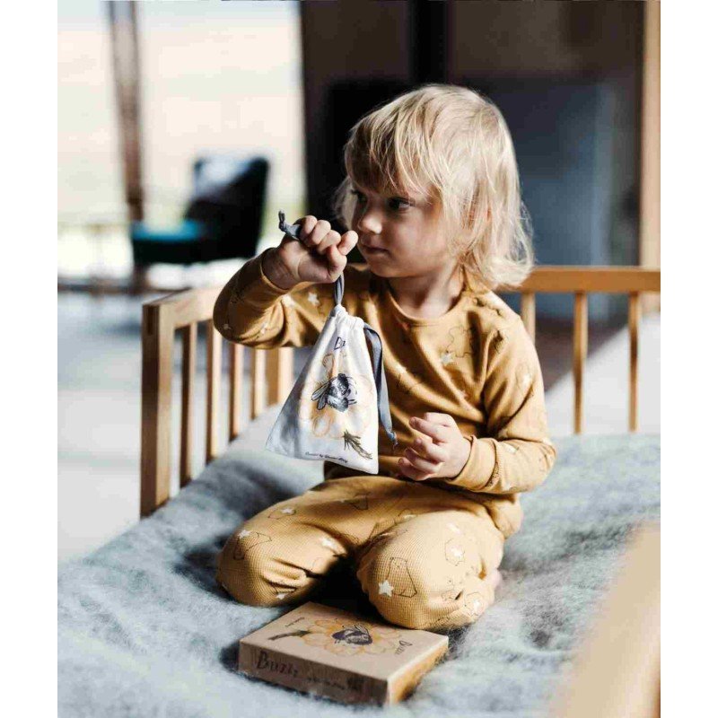 1. Child in yellow pajamas holding a bag with Wooden Buzz Spinner on a bed