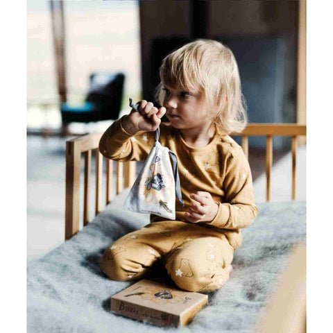 1. Child in yellow pajamas holding a bag with Wooden Buzz Spinner on a bed