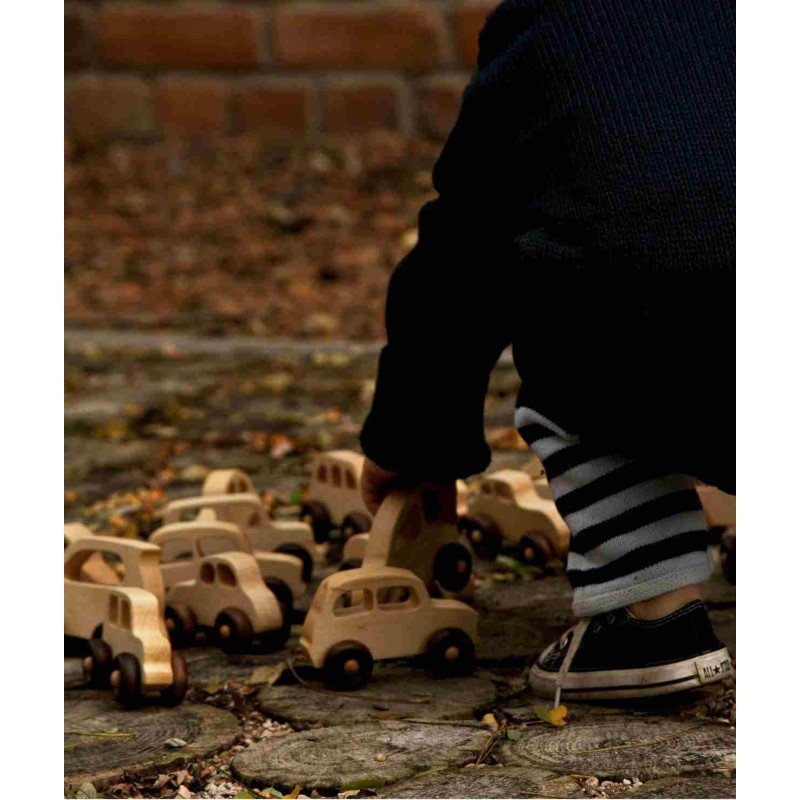 1. Child arranging eco-friendly wooden toy cars on a stone path outdoors, wearing striped pants and sneakers