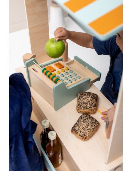 7. Child holding green apple while playing with wooden cash register