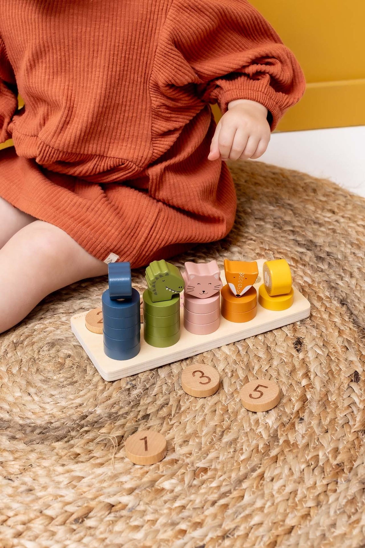 3. Child interacting with wooden counting puzzle on woven mat, featuring colorful animal figures
