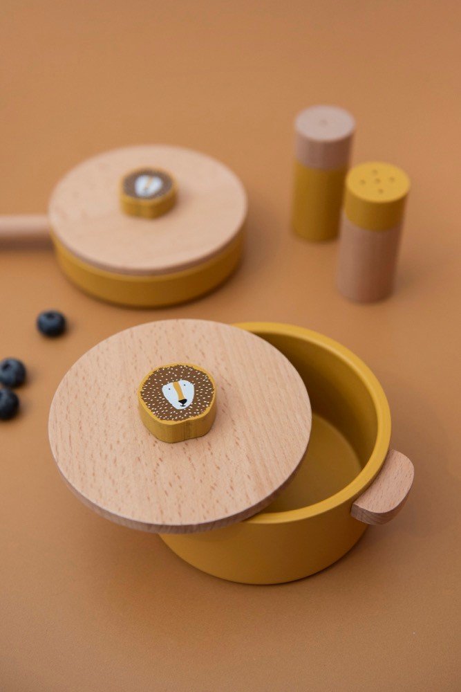 1. Lifestyle image of Trixie Baby Mr. Lion wooden kitchen set with pot, pan, and shakers on a warm-toned surface