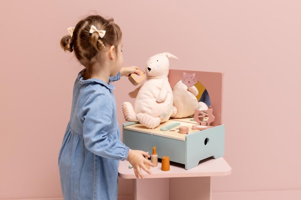 1. Young girl playing with Trixie Baby Wooden Make-Up Table featuring mirror, plush toy, and accessories in a pastel pink room
