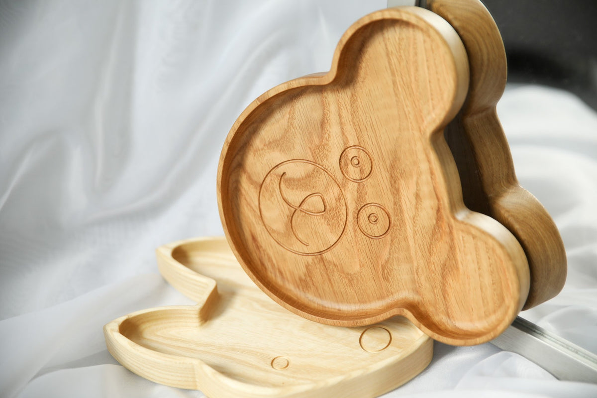9. Two wooden bear-shaped plates with engraved face design, displayed on white fabric