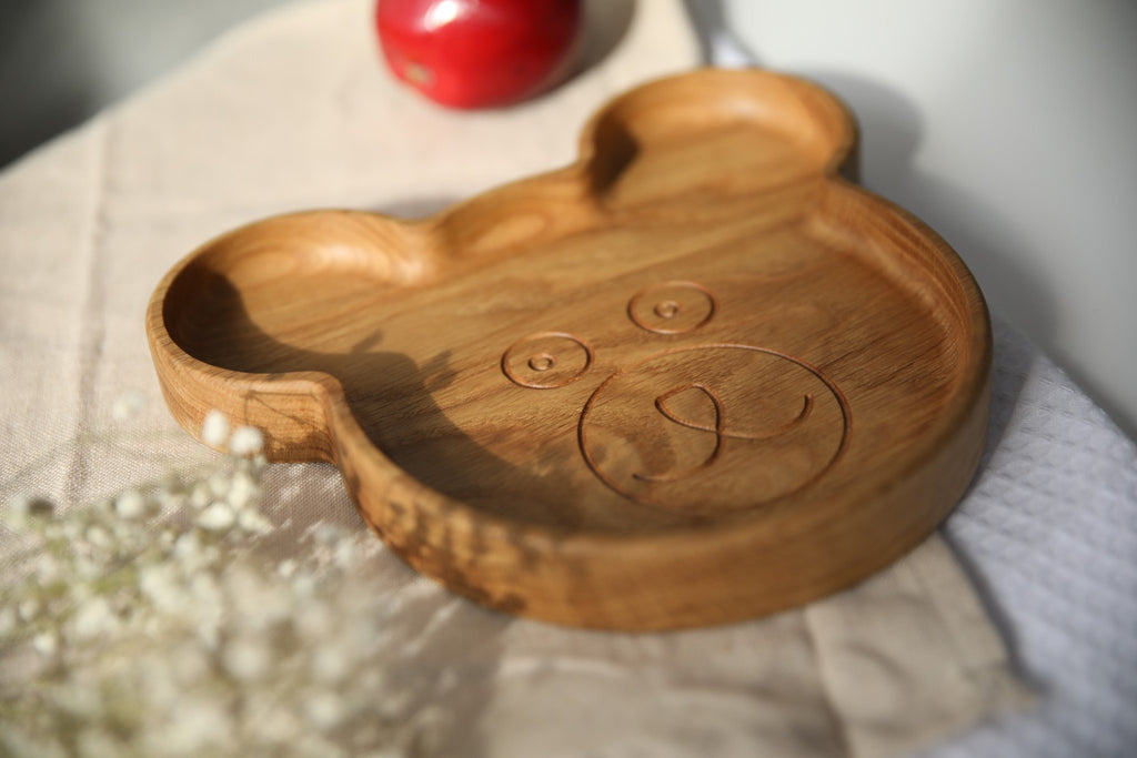 6. Wooden bear-shaped plate with engraved face, placed on beige cloth with red apple