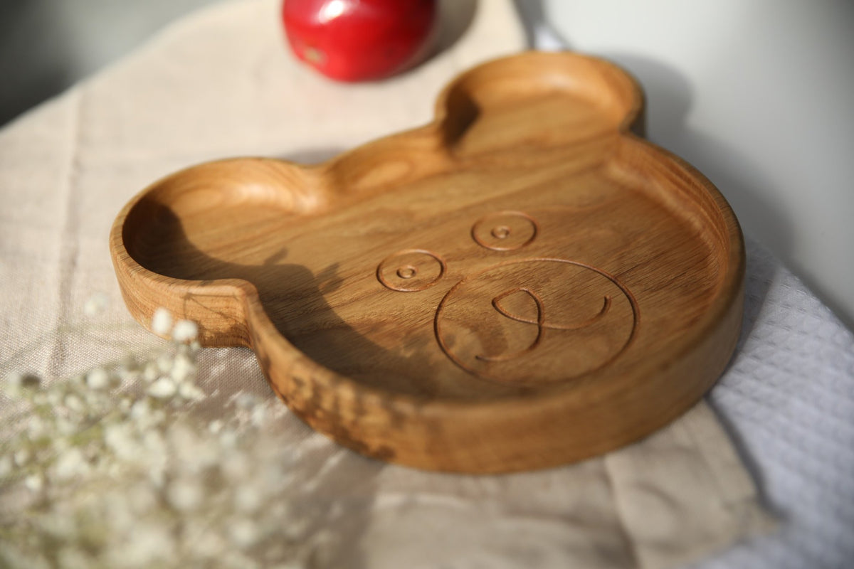 6. Wooden bear-shaped plate with engraved face, placed on beige cloth with red apple