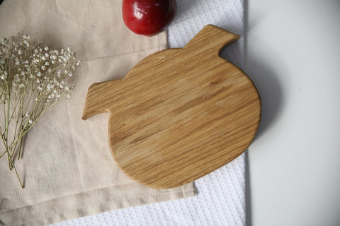 2. Back view of wooden boar-shaped plate for kids on a beige cloth with a red apple and white flowers, highlighting smooth finish
