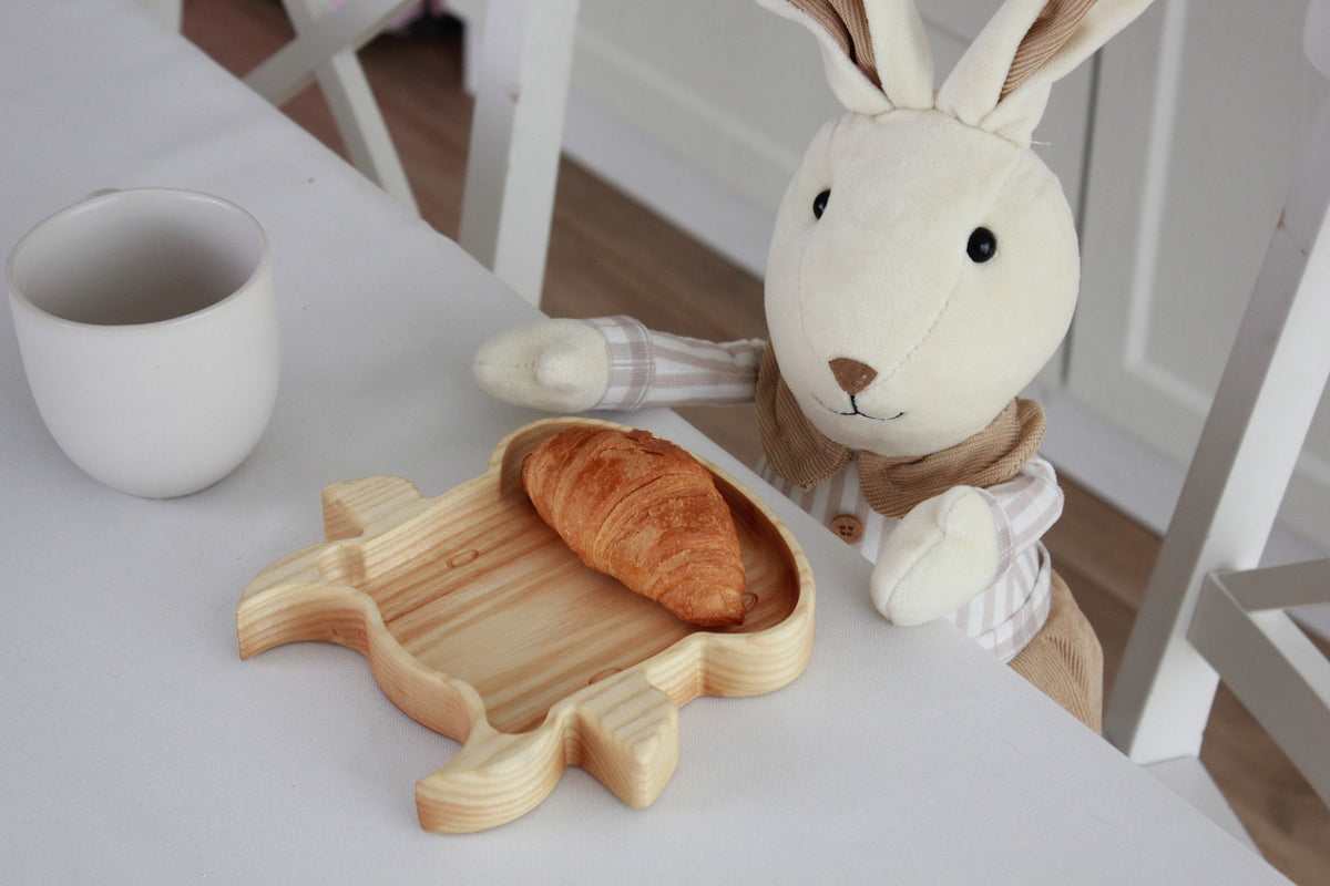 3. Stuffed rabbit toy beside wooden bull-shaped plate with croissant on dining table
