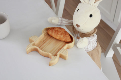 1. Plush rabbit toy next to wooden bull-shaped plate with croissant on white table