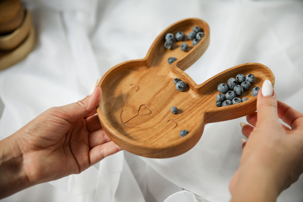 6. Oak wooden bunny plate with blueberries held by two hands on a white fabric