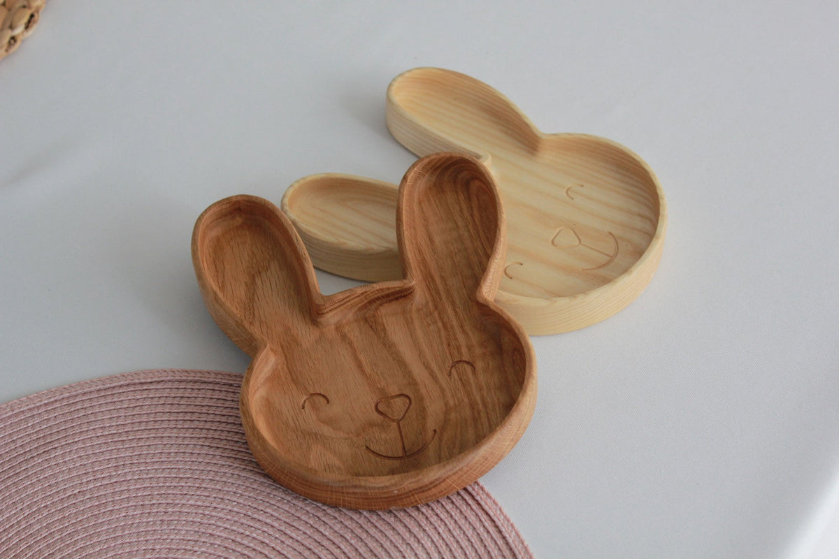 1. Two wooden bunny-shaped plates in oak and ash on a white surface with a pink woven mat