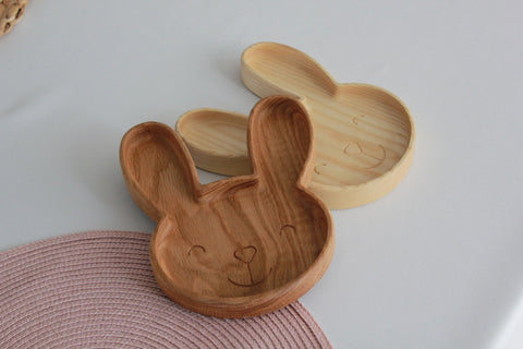 1. Two wooden bunny-shaped plates in oak and ash on a white surface with a pink woven mat