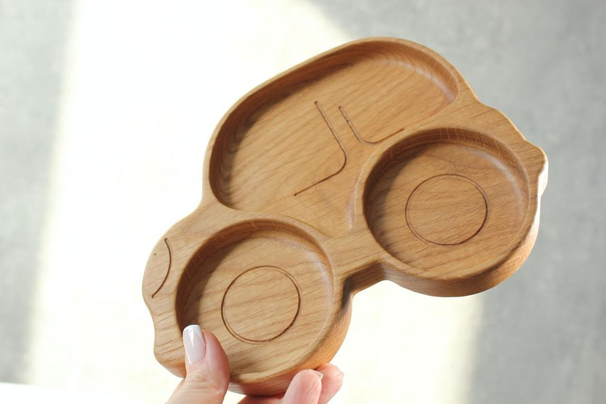 5. Hand holding wooden car-shaped plate for kids against a light background, showcasing its smooth, polished surface
