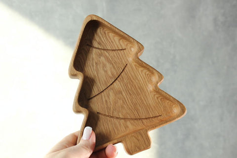1. Hand holding a handmade wooden plate shaped like a Christmas tree, made of oak or ash, against a neutral background