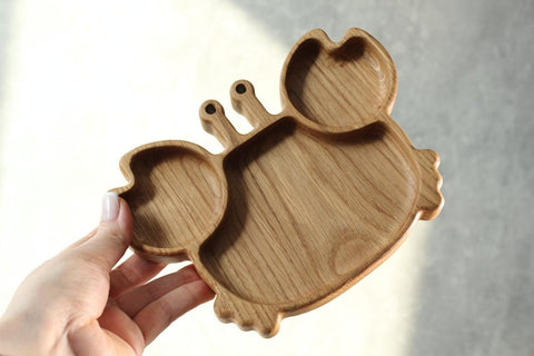 4. Hand holding oak wooden crab-shaped plate for kids, highlighting the size and smooth finish of the product