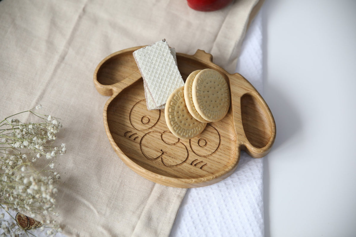 2. Wooden dog-shaped plate for kids with cookies and wafers, made from natural oak or ash, displayed on a beige cloth, showcasing its food-safe, polished finish.