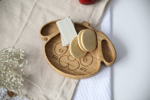 2. Wooden dog-shaped plate for kids with cookies and wafers, made from natural oak or ash, displayed on a beige cloth, showcasing its food-safe, polished finish.