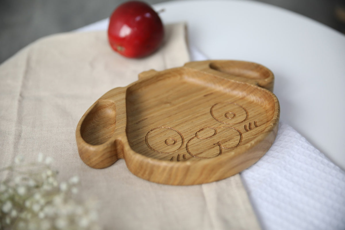 3. Close-up of wooden dog-shaped plate for kids, made from natural oak or ash, on a beige cloth with a red apple, highlighting its smooth, hand-polished surface.