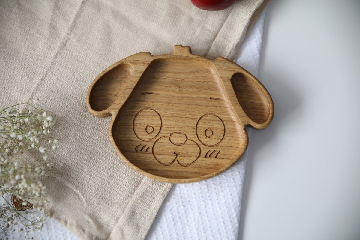 1. Handmade wooden plate for kids shaped like a dog, made from natural oak or ash, shown on a beige cloth with flowers, highlighting its smooth, polished surface.