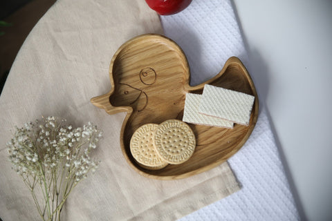 2. Wooden duckling plate with cookies and wafers on a beige cloth, accompanied by a red apple and white flowers